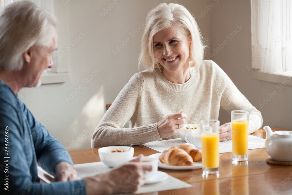 Happy aged husband and wife enjoy breakfast spending time at home together, senior couple eating healthy food smiling talking in morning, laughing elderly man and woman have tasty meal in kitchen Happy aged husband and wife enjoy breakfast spending time at home together, senior couple eating healthy food smiling talking in morning, laughing elderly man and woman have tasty meal in kitchen