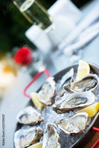 Fresh oysters with lemon's slices in ice and champagne. Restaurant delicacy, beautiful table setting. Saltwater oysters dish.