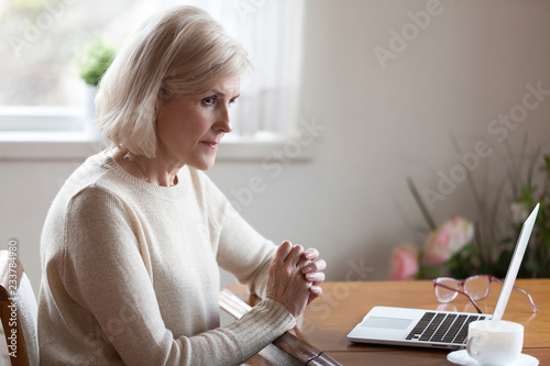 Fotografia Thoughtful aged woman working at laptop thinking or considering something, doubt