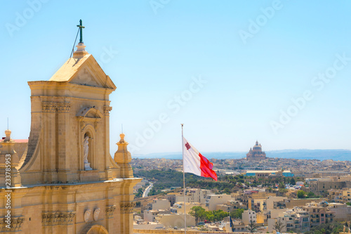 Capital city Victoria top view from Cathedral of the Assumption, Gozo with Maltese flag. Island city panorama on architecture and buildings from historic church. Summer colorful tourism landmark.