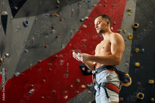 Low angle view of caucasian shirtless male rock climber applying chalk to his hand getting ready to climbing workout.