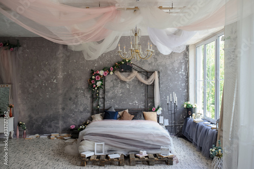 A wood bed in a photo studio decorated with flowers and curtains and sorrounded by books, frames, candle sticks photo