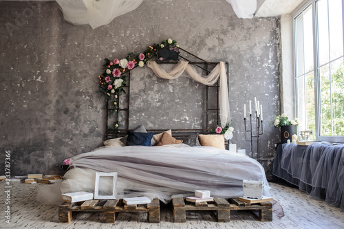 A wood bed in a photo studio decorated with flowers and curtains and sorrounded by books, frames, candle sticks photo