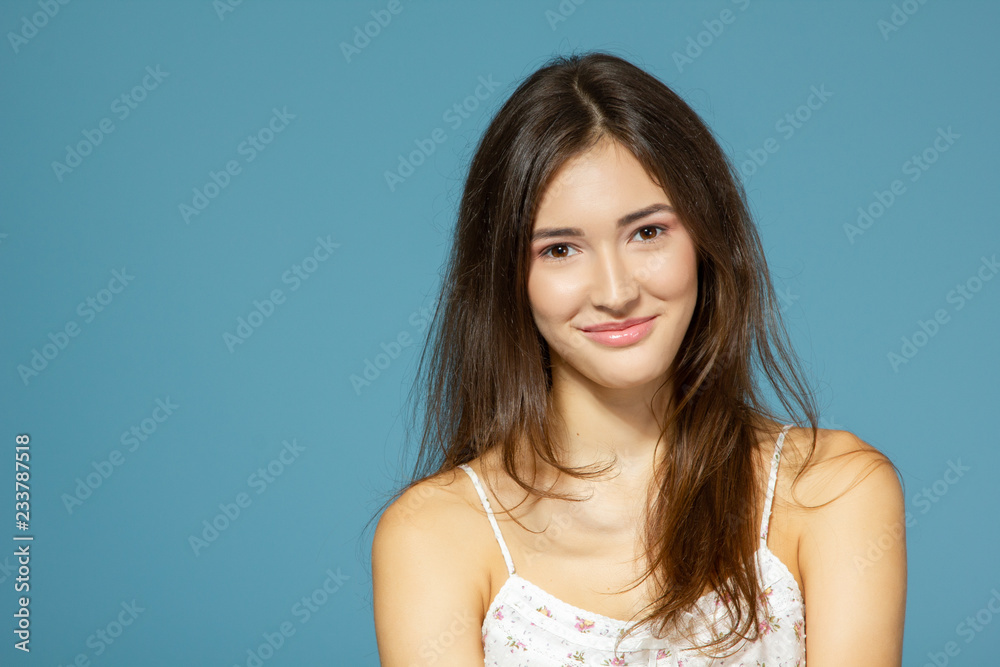 Beautiful calm teen girl looking at camera over blue background. Young pretty woman posinng at studio. Beautiful calm teen girl looking at camera over blue background. Young pretty woman posinng at studio.