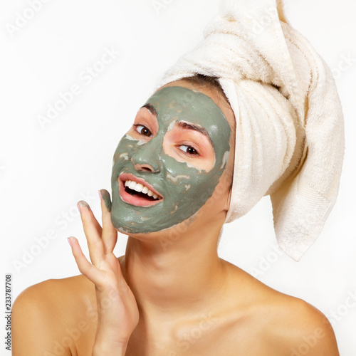 Beautiful cheerful teen girl applying facial clay mask. Beauty treatments, isolated over white background.