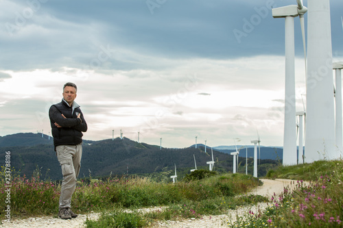 Man's portrait outdoor against blue sky with wind turbine. Windmill generators. Wind power generators.