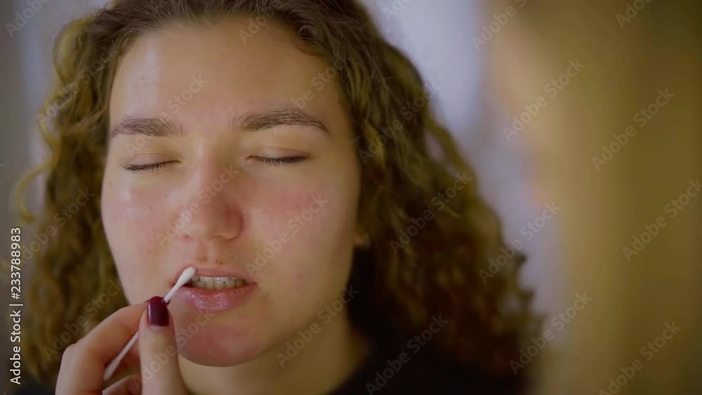 cosmetologist is covering lips of young female client by moisturizing balm using cotton stick cosmetologist is covering lips of young female client by moisturizing balm using cotton stick