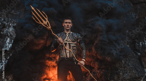 A young man with a trident against the background of fire and smoke. photo