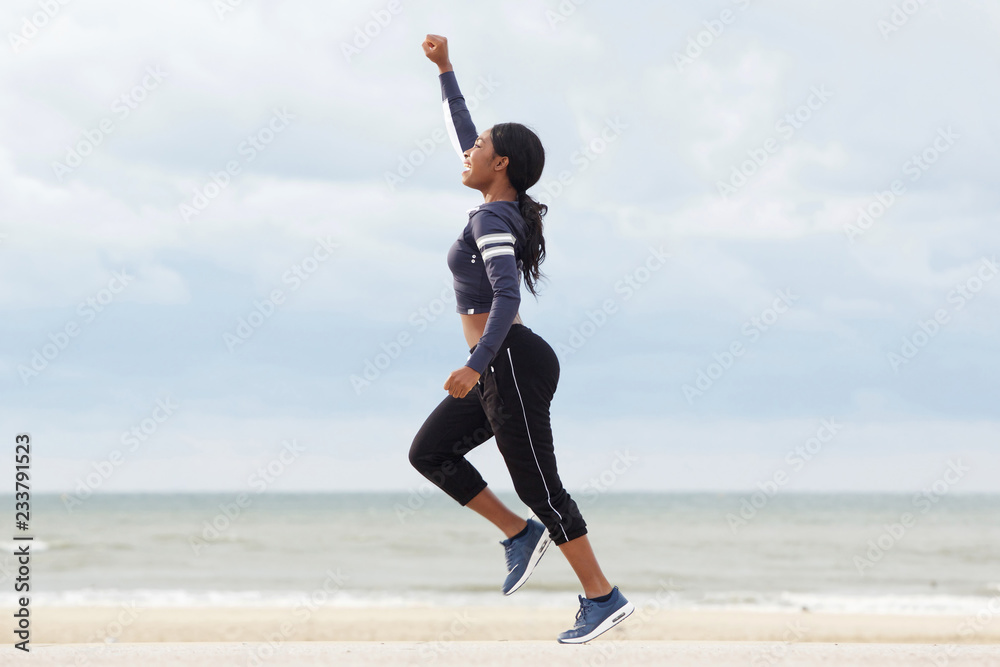 side portrait of young african american woman running with one arm raised at the beach side portrait of young african american woman running with one arm raised at the beach