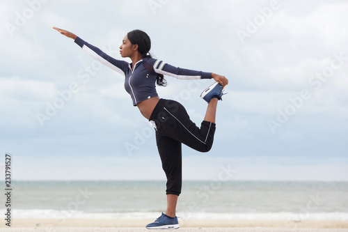 african american woman balancing on one leg at the beach