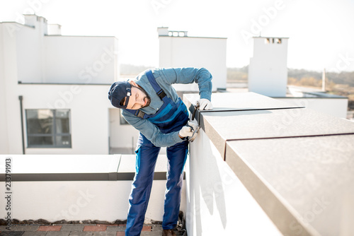 Builder in uniform mounting metal cover on the parapet of a new building