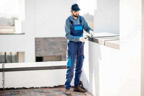 Builder in uniform mounting metal cover on the parapet of a new building photo