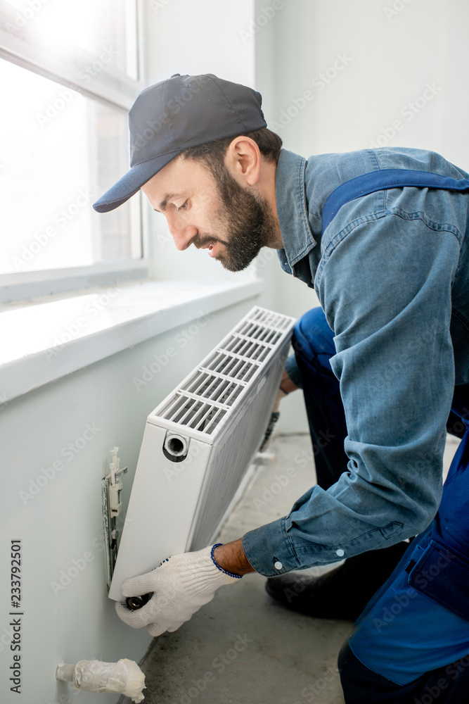 Workman mounting water heating radiator near the window in the white ...