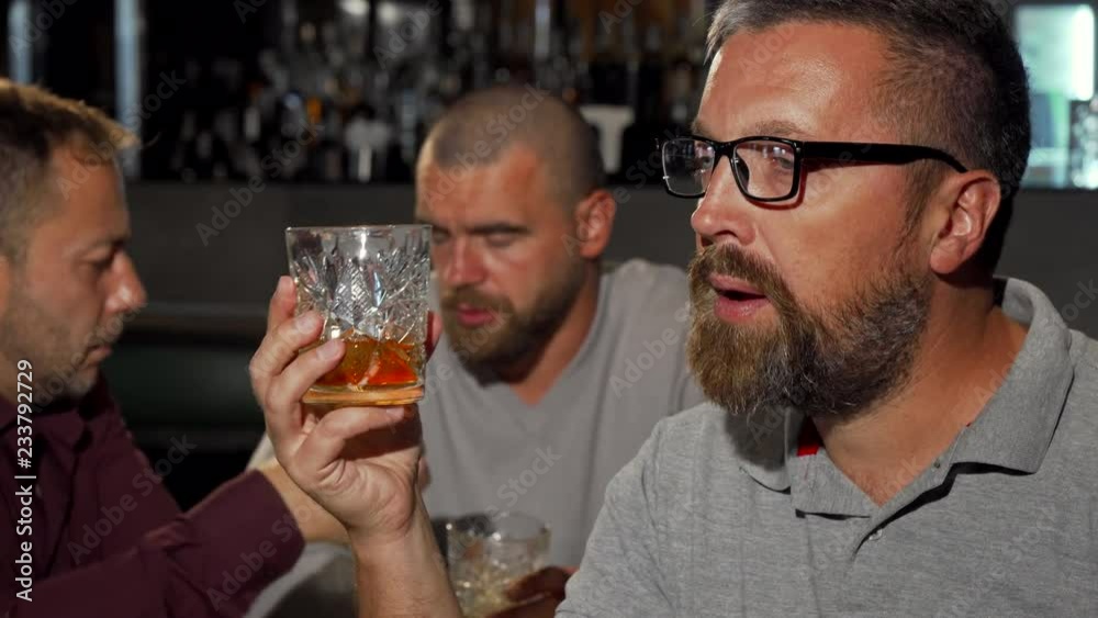 Bearded mature man smiling to the camera after tasting delicious whiskey. Group of mature men enjoying luxury alcohol drinks at the bar. Man tasting whiskey at the restaurant. Bearded mature man smiling to the camera after tasting delicious whiskey. Group of mature men enjoying luxury alcohol drinks at the bar. Man tasting whiskey at the restaurant.