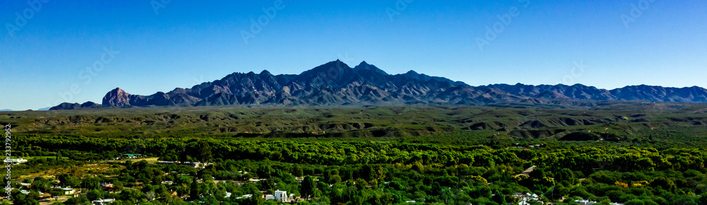 Aerial, drone view of Tubac, Arizona with blue sky, green flora including palo verde trees, purple mountains