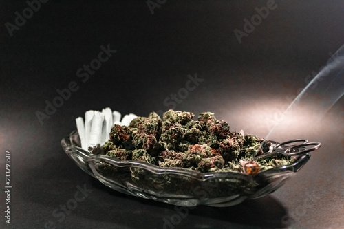 Obraz na płótnie Classy glass dish with marijuana bud, scissors and a dozen joints with one burning on black with spot lighting w salonie