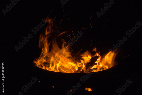 Beautiful flame with sparks in bonfire in the night. Heat and danger energy concept. Fire in darkness. Inferno and element concept. Campfire with bright flame. Fire in motion. 