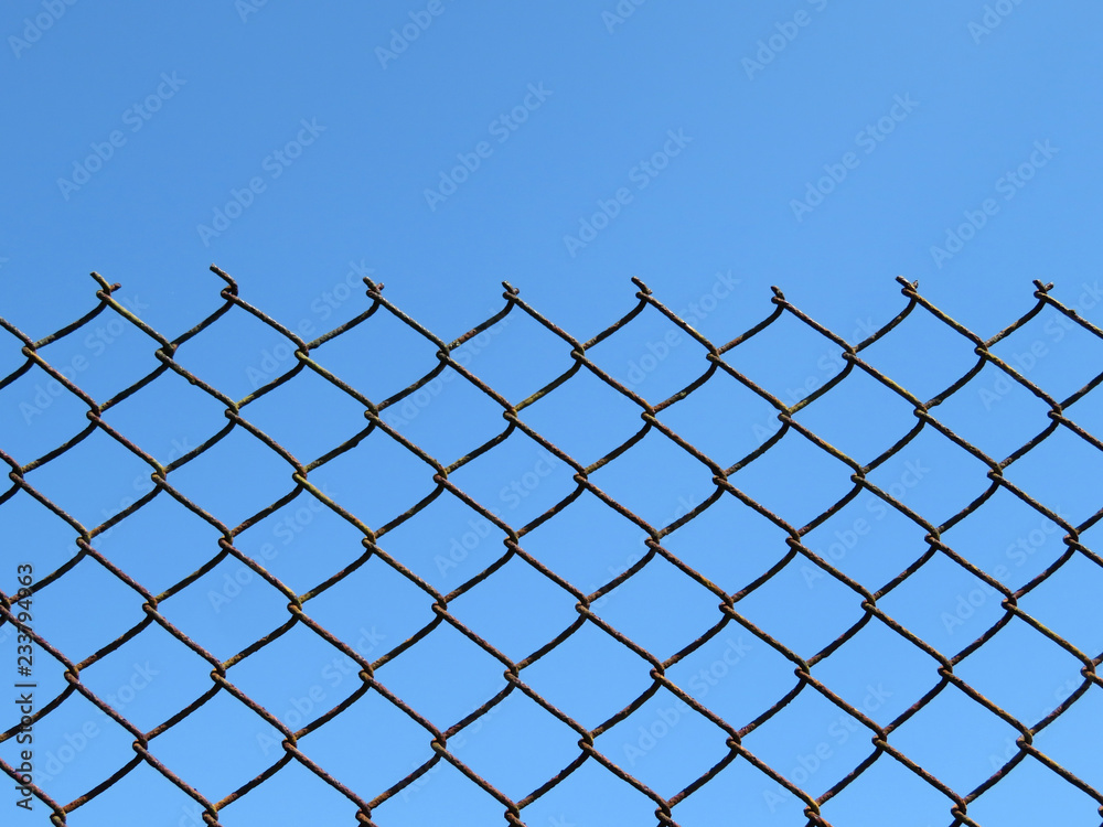 Wire mesh on clear blue sky background. Rusty wired fence, metallic net, isolated grid Wire mesh on clear blue sky background. Rusty wired fence, metallic net, isolated grid