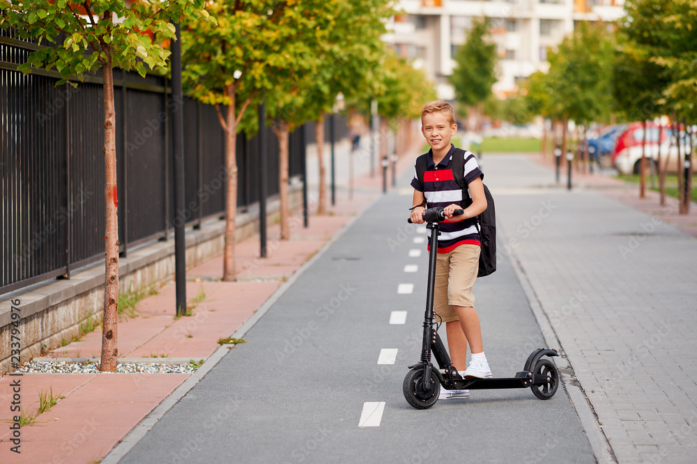 School boy in riding with his electric scooter in the city with backpack on  sunny day. Child in colorful clothes biking on way to school foto de Stock  | Adobe Stock