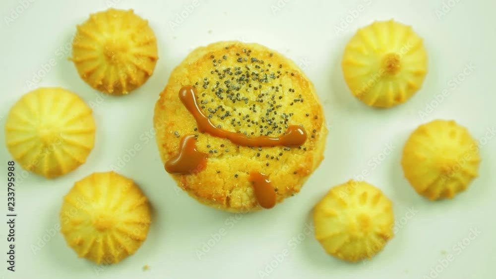 Butter biscuits with culinary paint painted with a funny emoticon and surrounded by small cookies. Movement in a circle Butter biscuits with culinary paint painted with a funny emoticon and surrounded by small cookies. Movement in a circle
