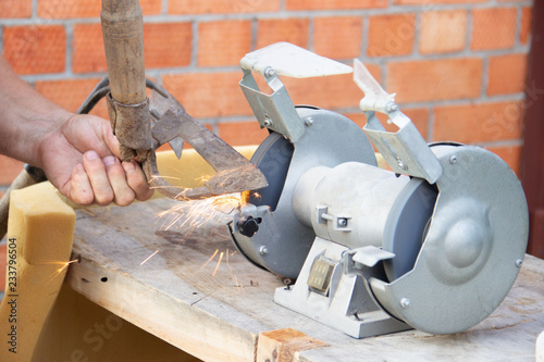 mans hand sharpens a hoe on electric grindstone in rural shed photo