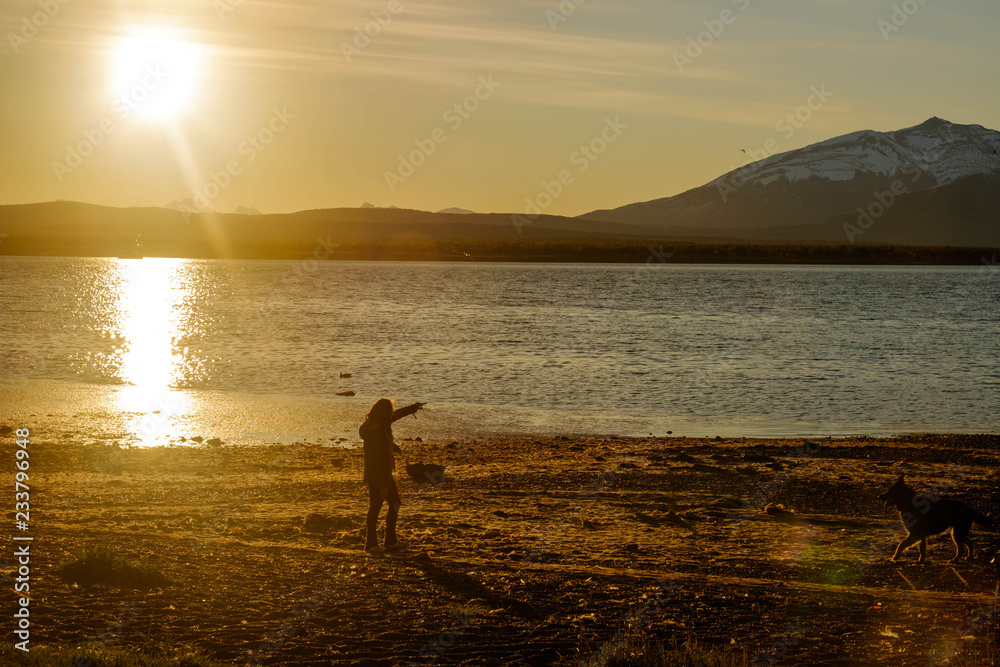 Fototapeta premium Girl and dog enjoying sunset at the beach of Puerto Natales, Patagonia, Chile