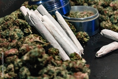 Marijuana joints surrounded by a large pile of bud and a bud grinder.
