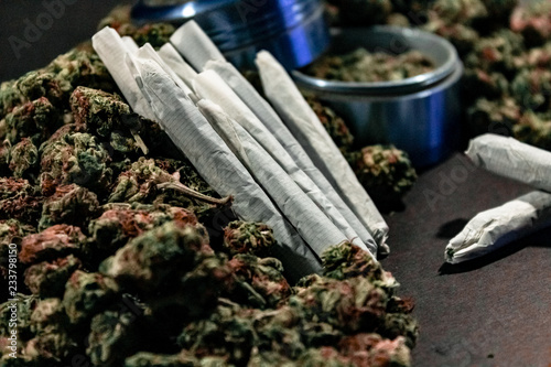 Marijuana joints surrounded by a large pile of bud and a bud grinder.