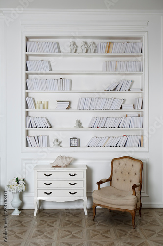 Interior of hite roomwith bookshelves, armchair and a chest of drawers. photo