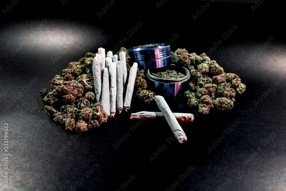 Marijuana joints stacked on a pile of bud with a blue coloured bud grinder.