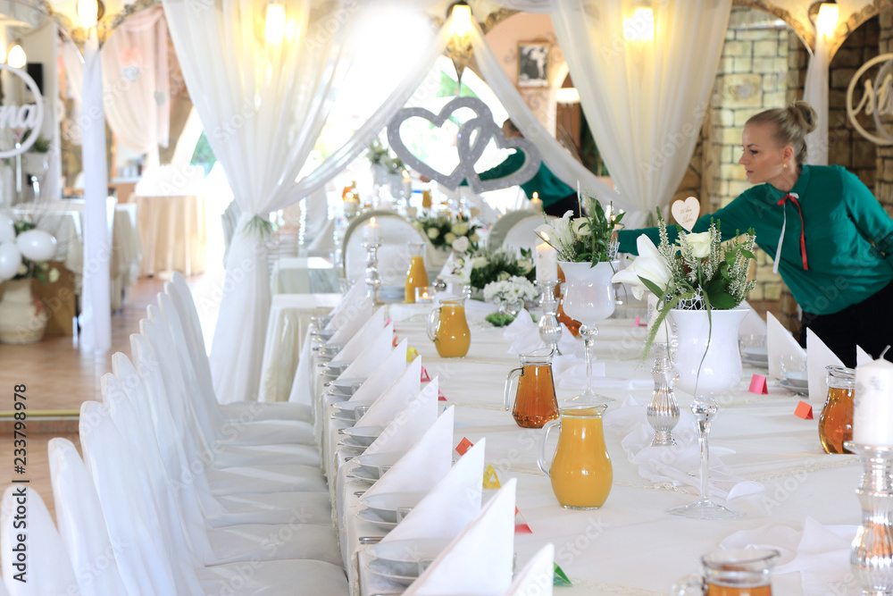 Kelnerka dekoruje stół w restauracji nakryty białym obrusem, ślub, wesele.	 - obrazy, fototapety, plakaty 