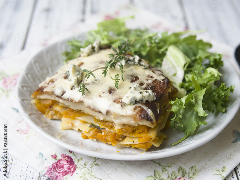 Slice of Pumpkin and Spinach Lasagne with blue cheese and salad on a White Wooden Table. Selective focus, copy space, closeup