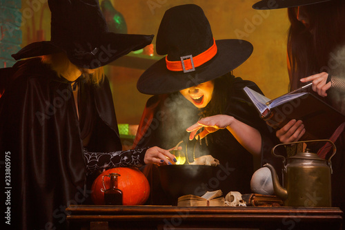 Photo of three witches in hats cooking poison in cauldron at dark room
