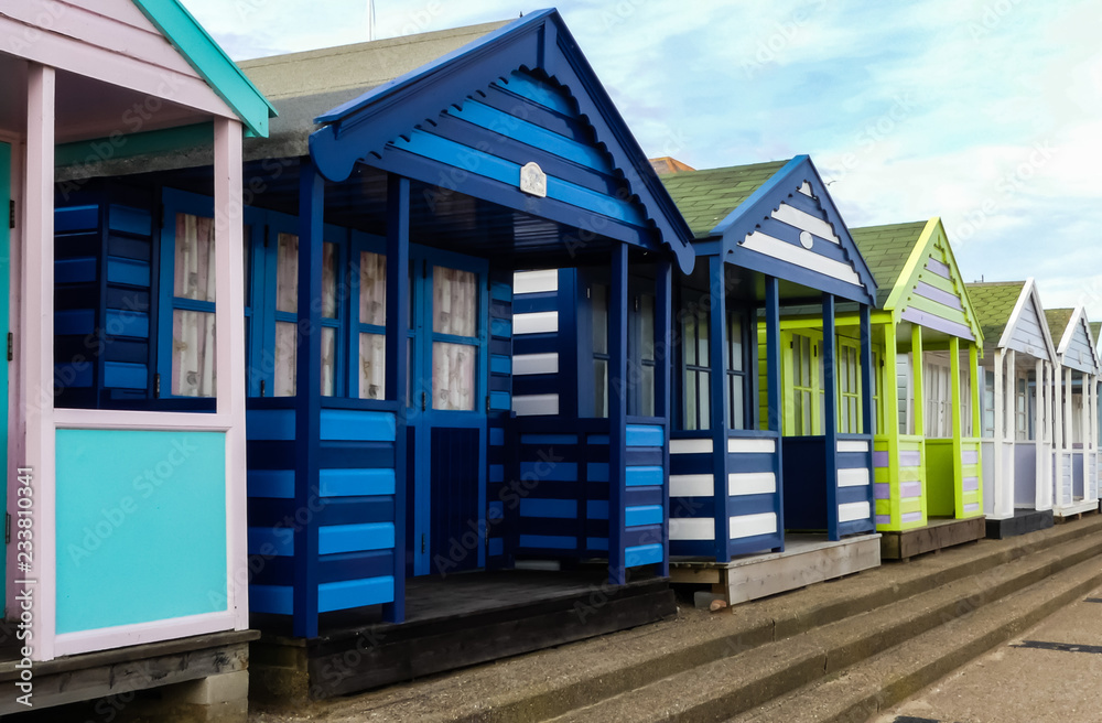 Colourfully painted generic wooden beach huts along a promenade, with steps down to a promenade. Blue sky with white clouds. England. Colourfully painted generic wooden beach huts along a promenade, with steps down to a promenade. Blue sky with white clouds. England.
