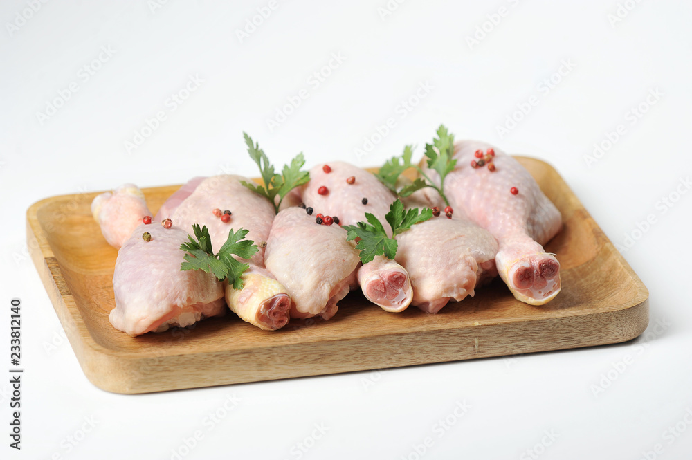 Raw chicken drumstick on a light wooden tray. Chicken legs are decorated with parsley and spices. White background. Close-up. Raw chicken drumstick on a light wooden tray. Chicken legs are decorated with parsley and spices. White background. Close-up.