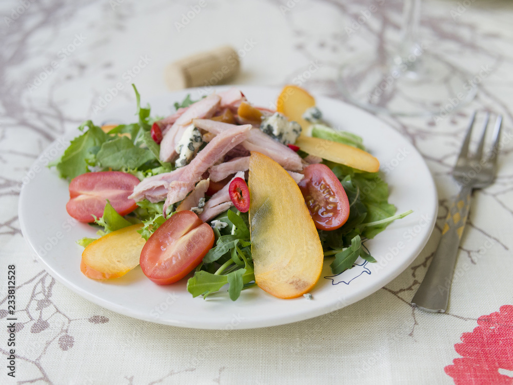 Salad with persimmon, smoked chicken, cherry tomatoes, Camembert cheese and blue cheese sauce. Festive dish . Christmas dinner. Selective focus, closeup, copy space