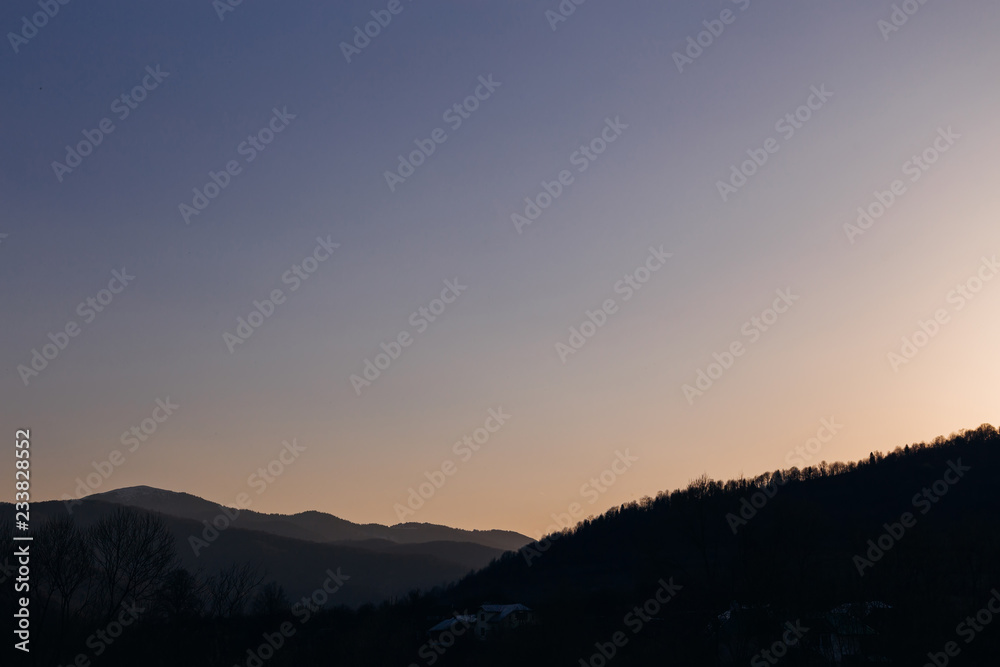 evening sky and silhouettes of mountain peaks and several buildings on the slopes of the mountain