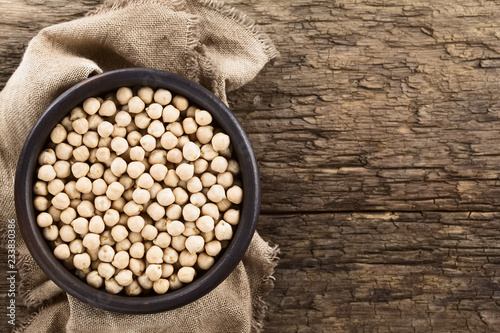 Raw chickpeas or garbanzo beans (lat. Cicer arietinum) in rustic bowl, photographed overhead on rustic wood with copy space on the side (Selective Focus, Focus on the chickpeas) photo