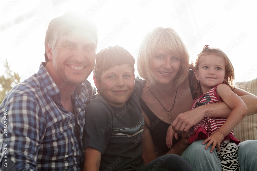 family with two children sitting together and looking at camera family with two children sitting together and looking at camera