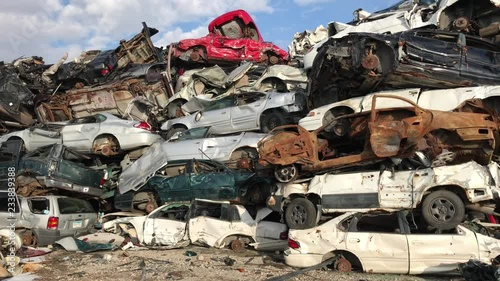 Cars in scrap yard stacked up in sunlight with varying colors and conditions; pan from left to right.
