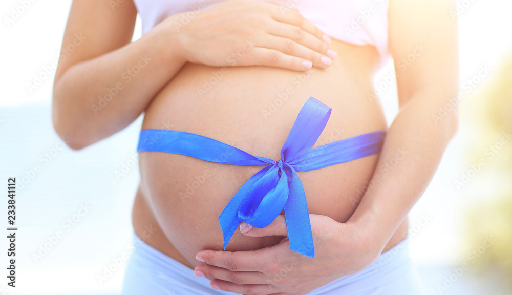 closeup of a pregnant woman tying a blue ribbon on her belly closeup of a pregnant woman tying a blue ribbon on her belly