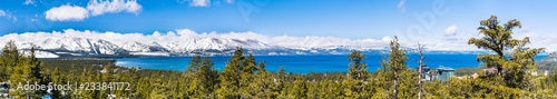 Panoramiczny widok w kierunku jeziora Tahoe w słoneczny, pogodny dzień; w tle pokryte śniegiem góry Sierra; wiecznie zielone lasy na pierwszym planie