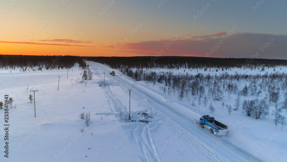AERIAL: Snowplow driving and plowing through snow covered highway amidst forest