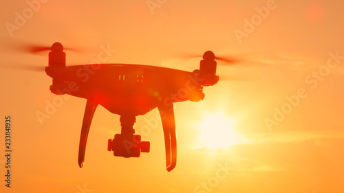 SILHOUETTE: Quadcopter drone flying towards camera at golden sunset