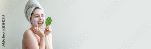 Bild auf Leinwand Beauty portrait of woman in towel on head with white nourishing mask or creme on face and green leaf in hand, white background isolated