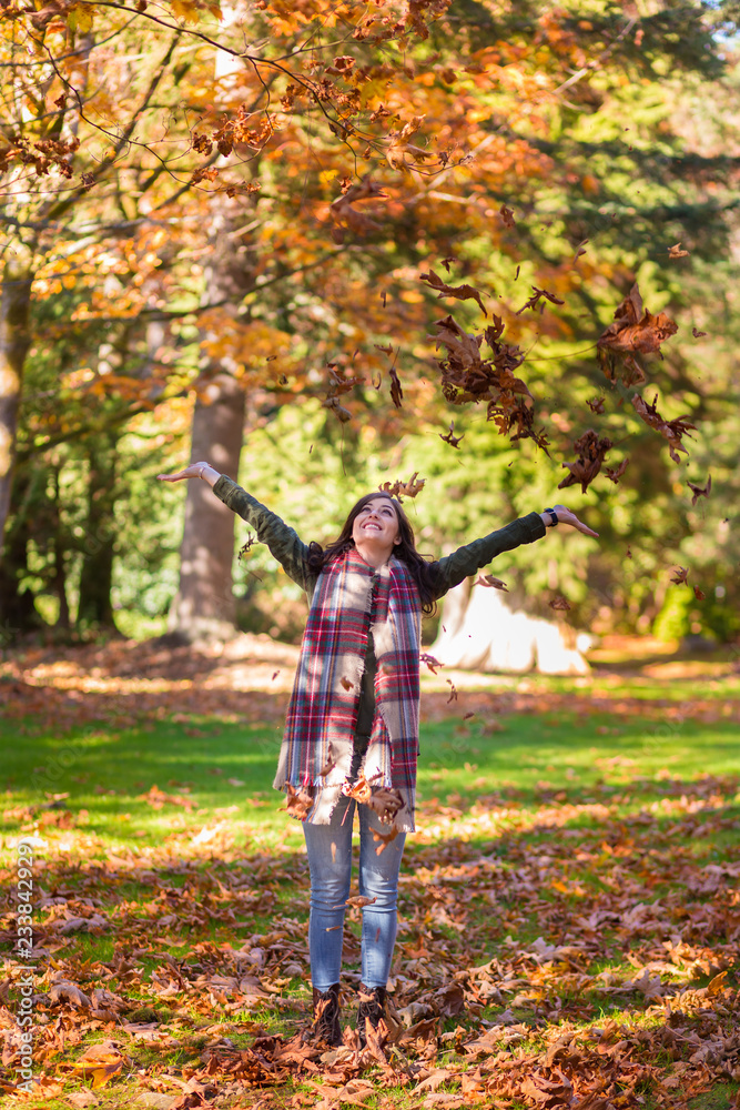 A young brunette woman throwing fall leaves into the air.