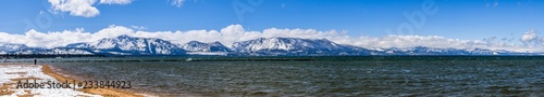 South Lake Tahoe shoreline and snow covered sandy beach, on a sunny day; the snow covered Sierra mountains in the background; California