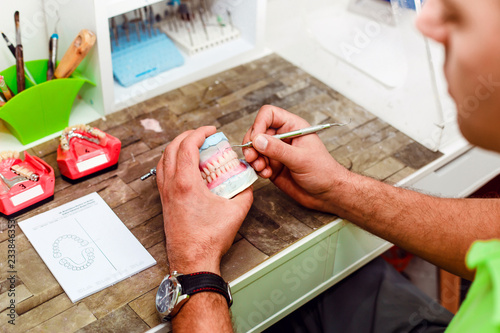 Dental technician using a knife with ceramic dental implants in his laboratory. Dentist working with tooth dentures in his lab office