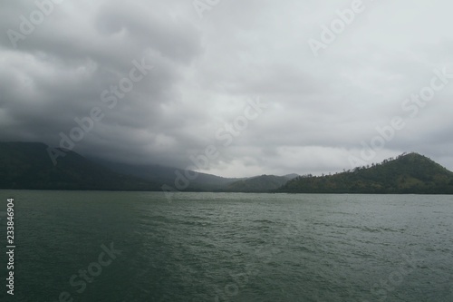 Overcast sky with heavy clouds over sea with signs of storm approaching with hills on background 