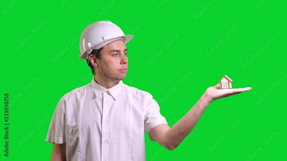 Young male engineer standing and showing hand palm with small model of house on green screen background Young male engineer standing and showing hand palm with small model of house on green screen background